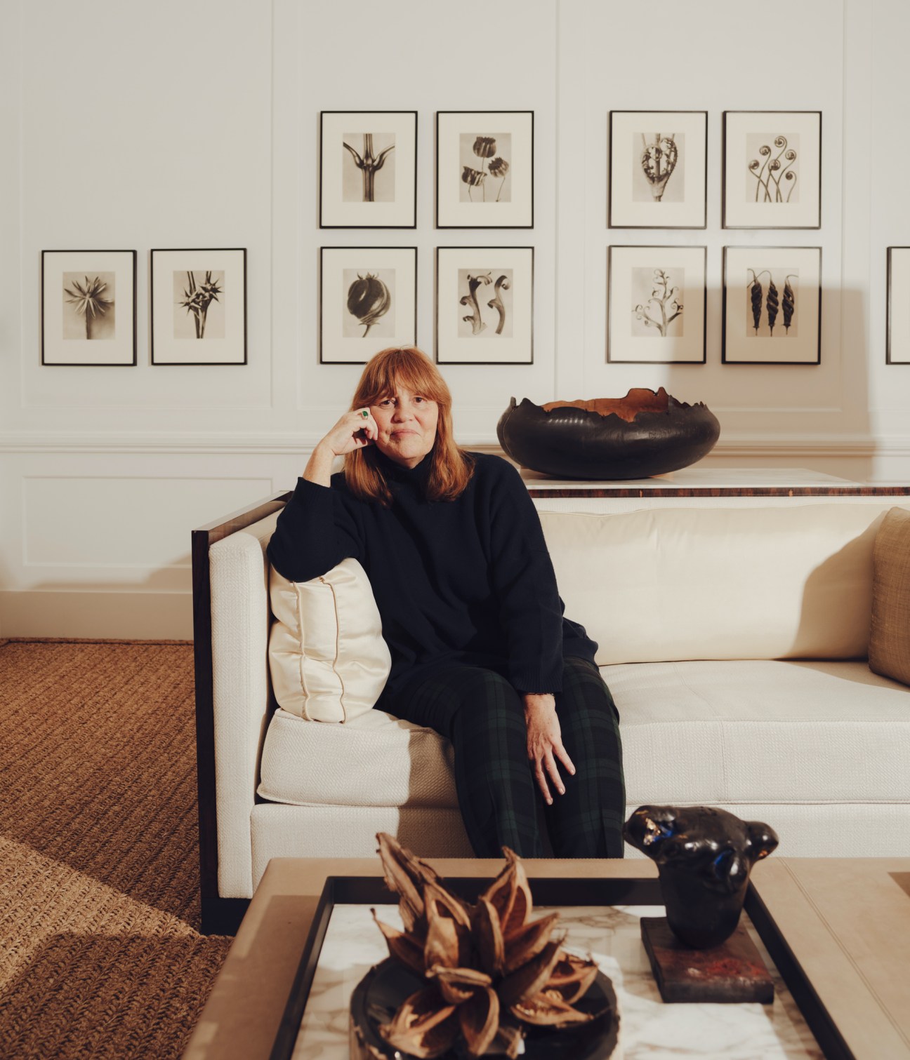 Isabel Ettedgui sitting in a cream leather armchair in her light-filled townhouse with framed botanical artwork on the wall