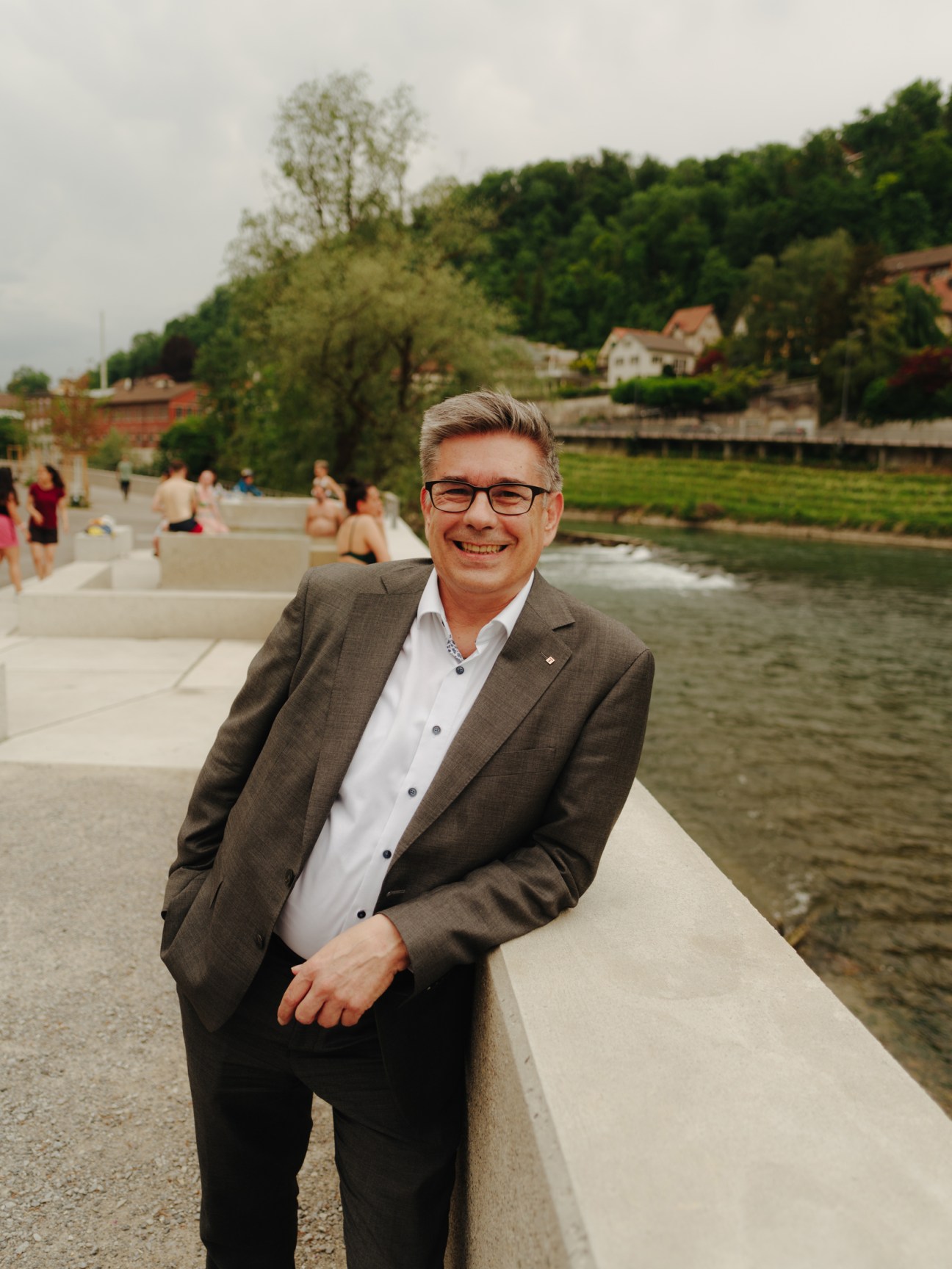 Markus Schneider, mayor of Baden, smiling in a suit jacket while sitting by the Limmat river waterfront