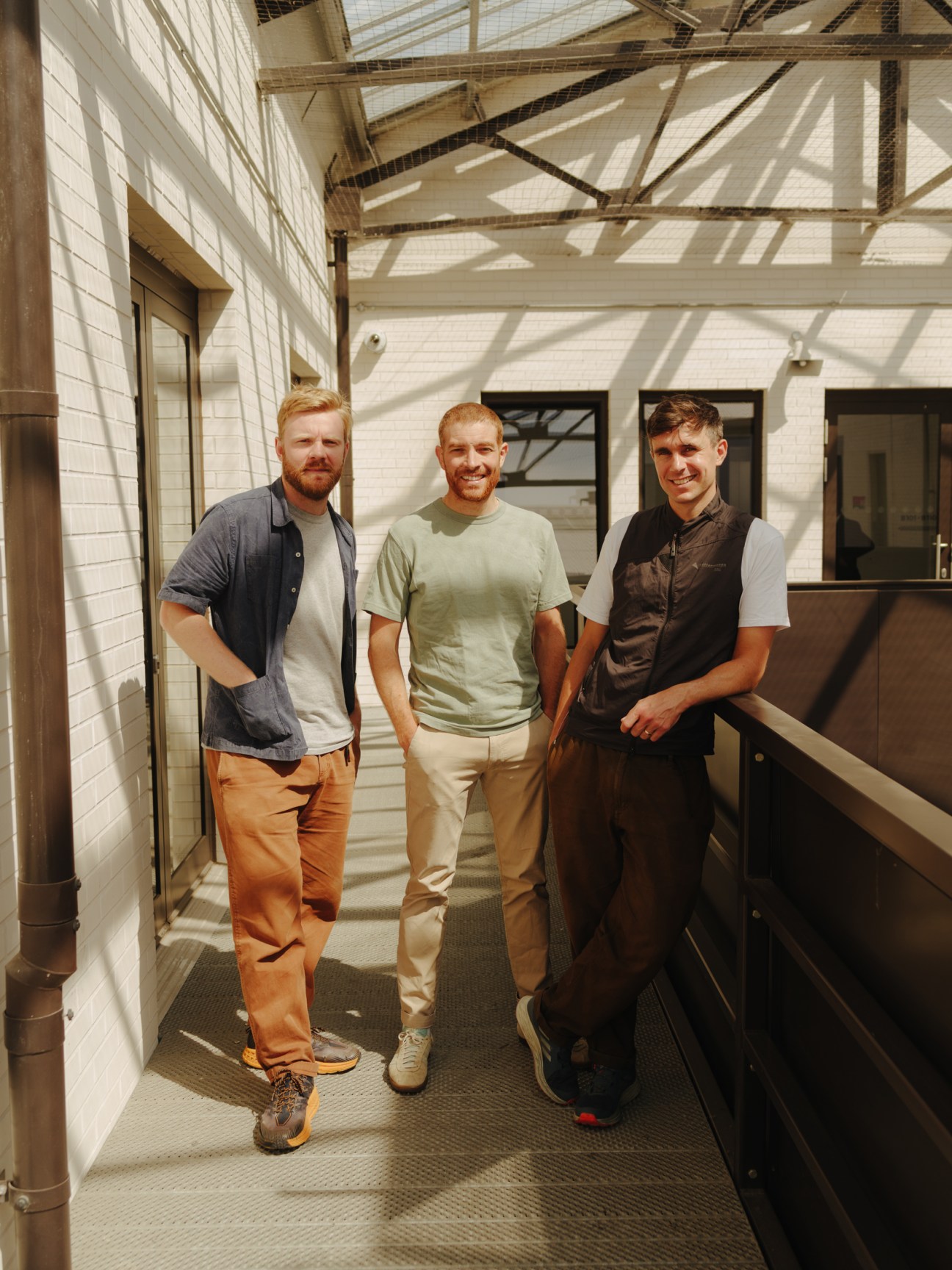 Three men standing together on an industrial walkway with white brick walls and metal framework overhead, Albion co-founders Charlie Stewart, Rupert Hartley and Jack Howker.