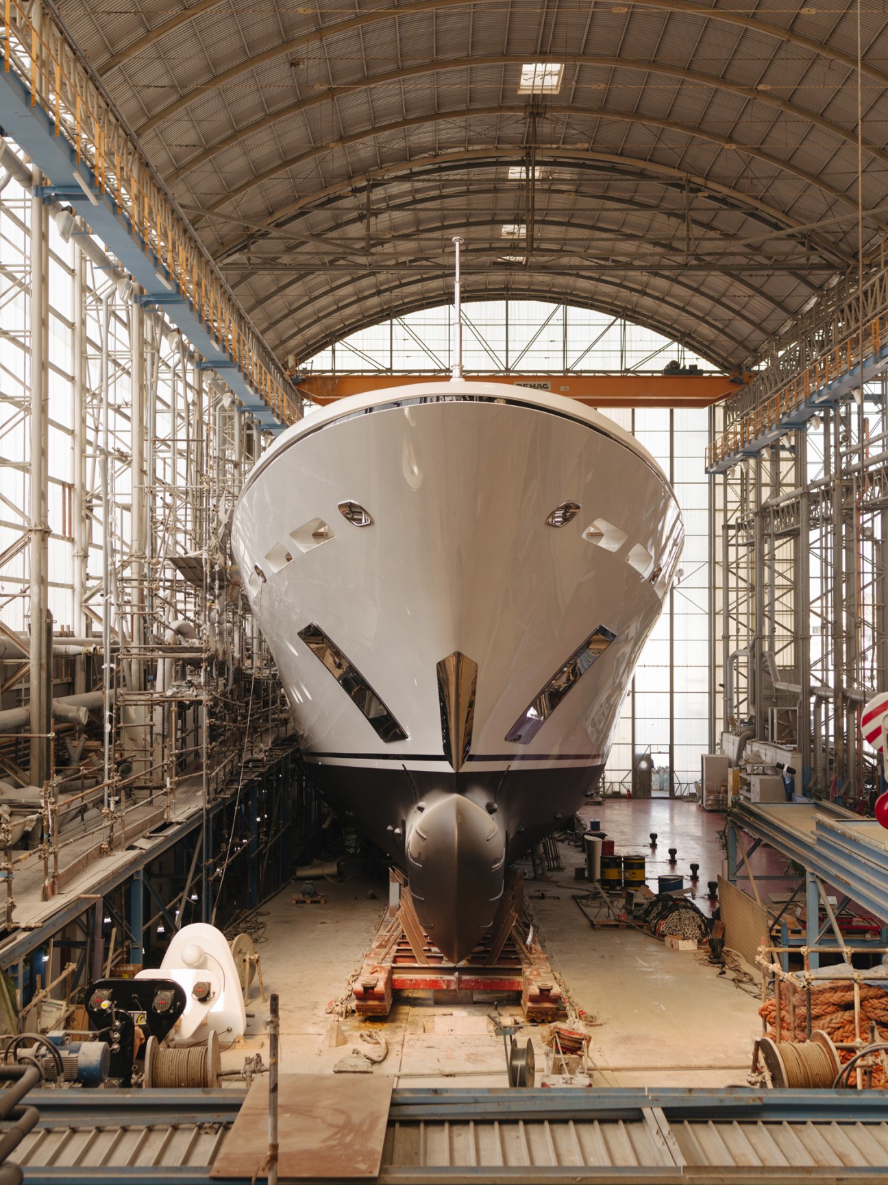 Large white yacht under construction in industrial shipyard hangar with scaffolding and equipment