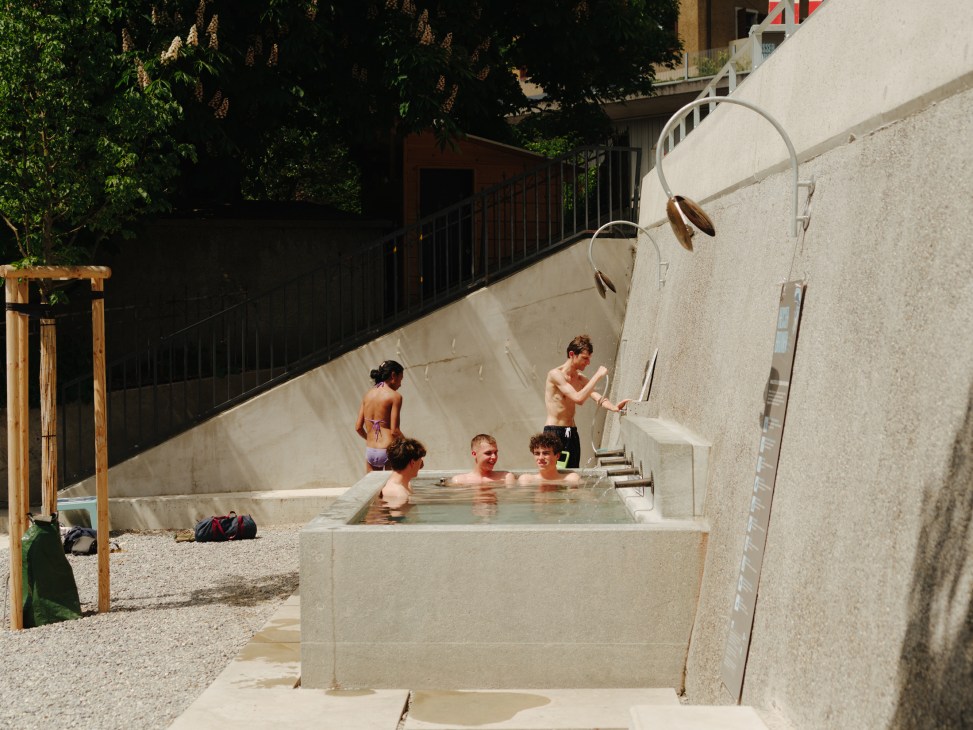 People enjoying thermal baths in stone pools under trees with concrete walls and metal handrails