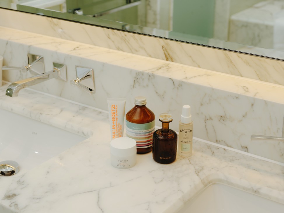 Skincare and grooming products arranged on marble bathroom counter including bottles and tubes