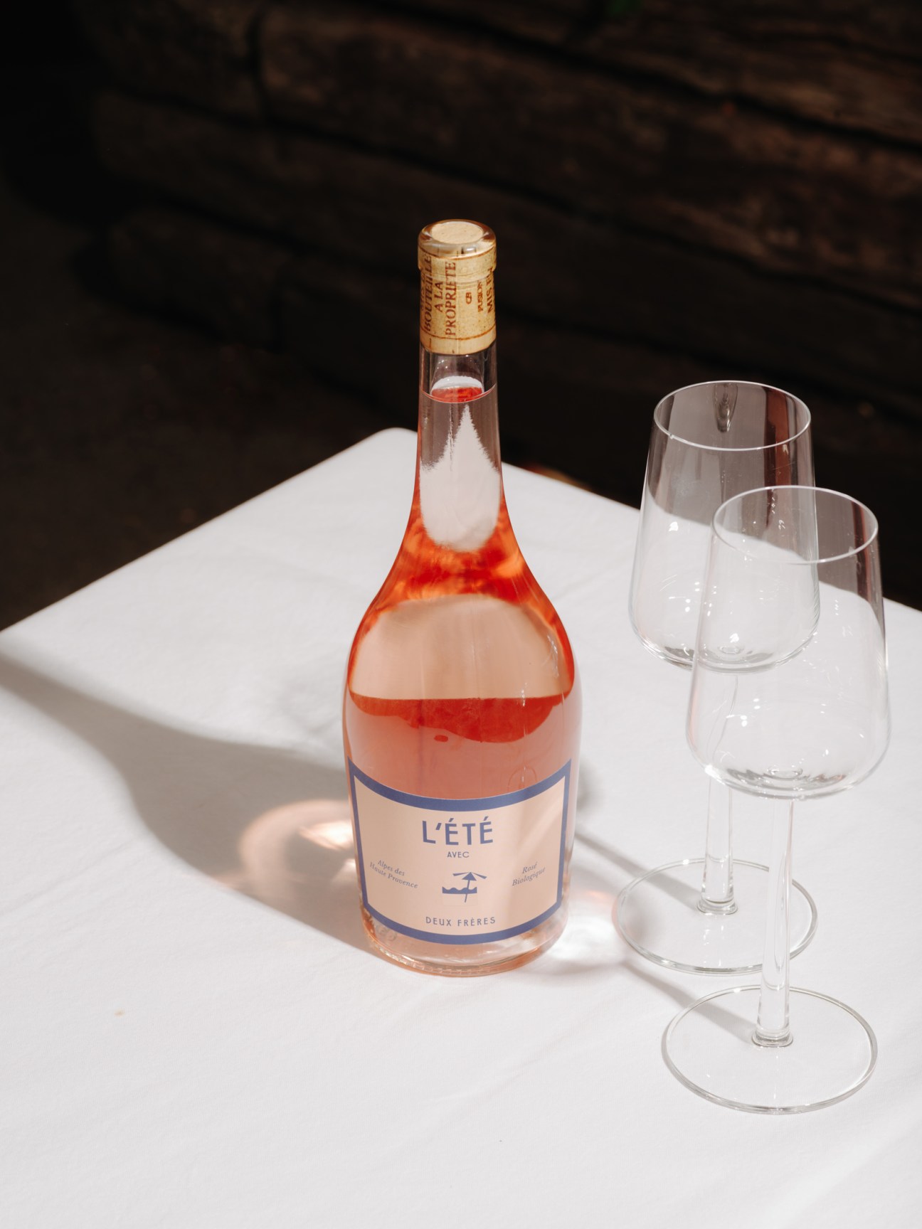 L'Été rosé wine bottle by Deux Frères with two empty wine glasses on white surface