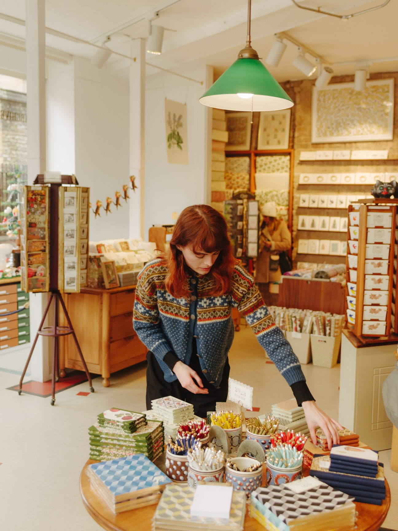 Woman in patterned cardigan arranging stationery products on a round table in Choosing Keeping store