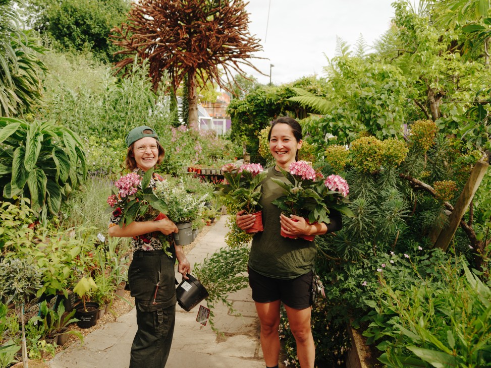Two women volunteers smiling and holding pink flowering plants at Walworth Garden community organic garden