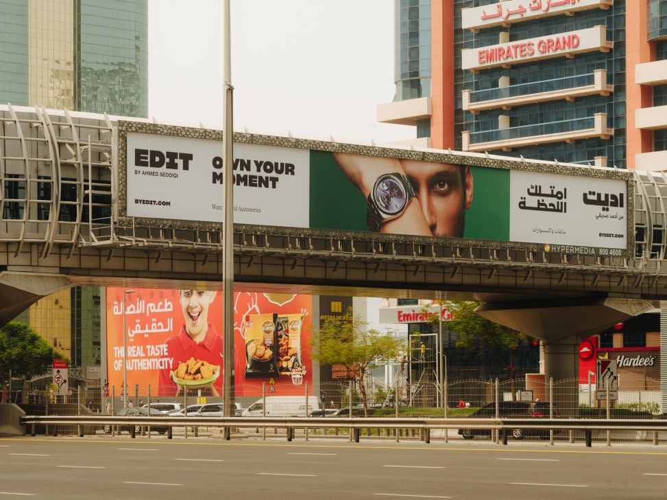 Multiple billboards and advertisements displayed along a Dubai motorway overpass, including fashion and food brand ads.