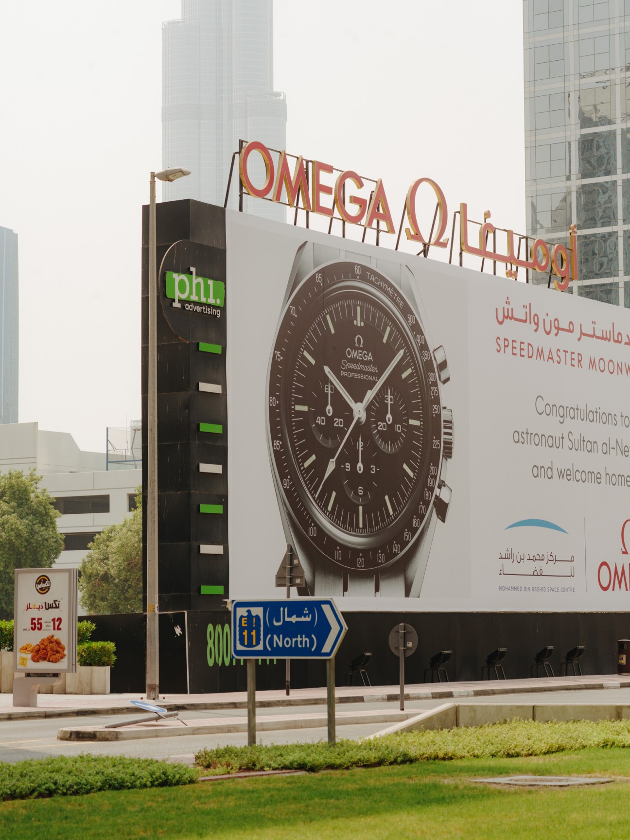 Large billboard featuring an Omega Speedmaster watch advertisement in Dubai with Arabic and English text.