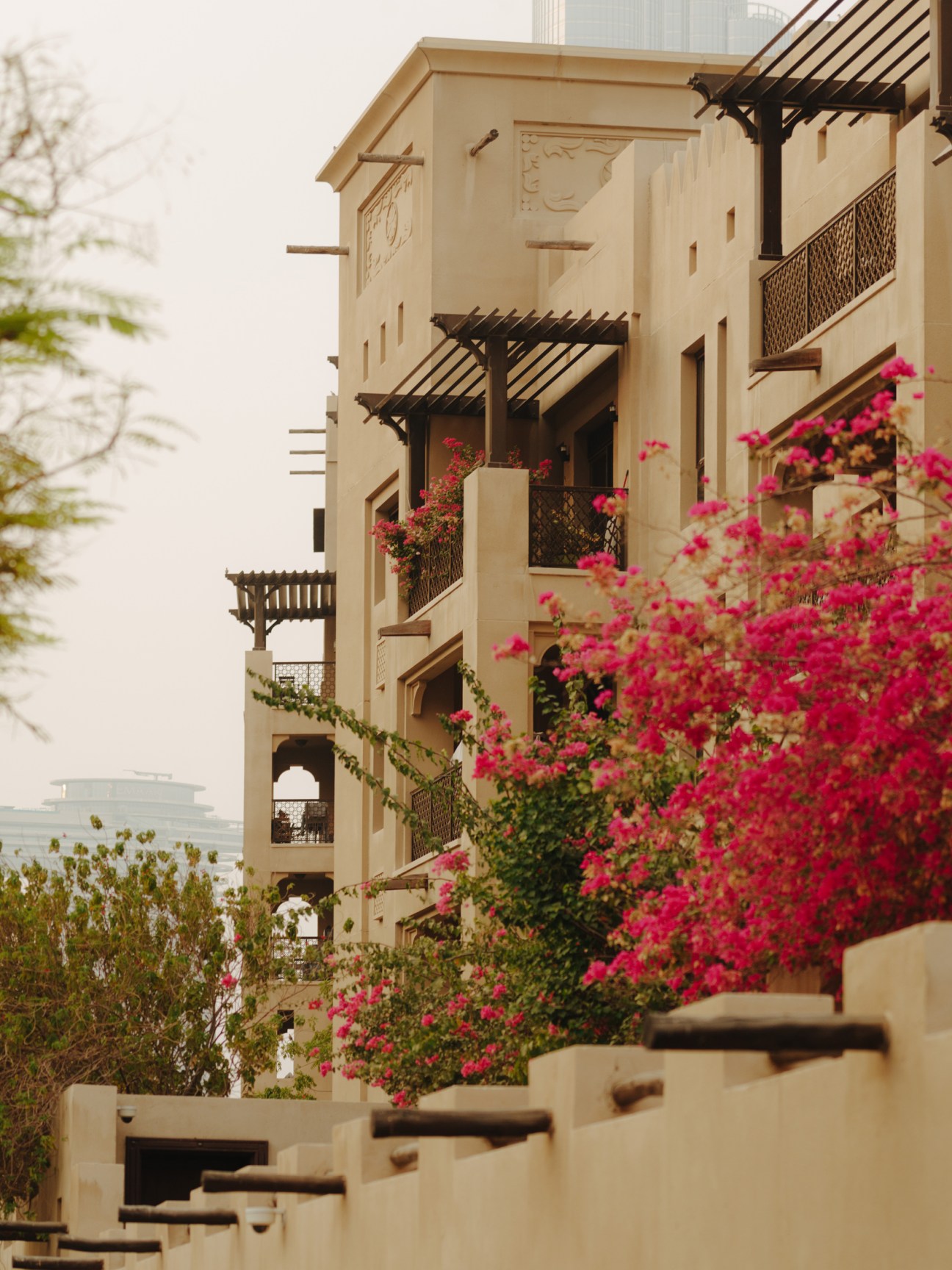 Traditional-style residential building in Old Town Dubai with cream-colored architecture, wooden pergolas, and vibrant pink bougainvillea flowers in planters.