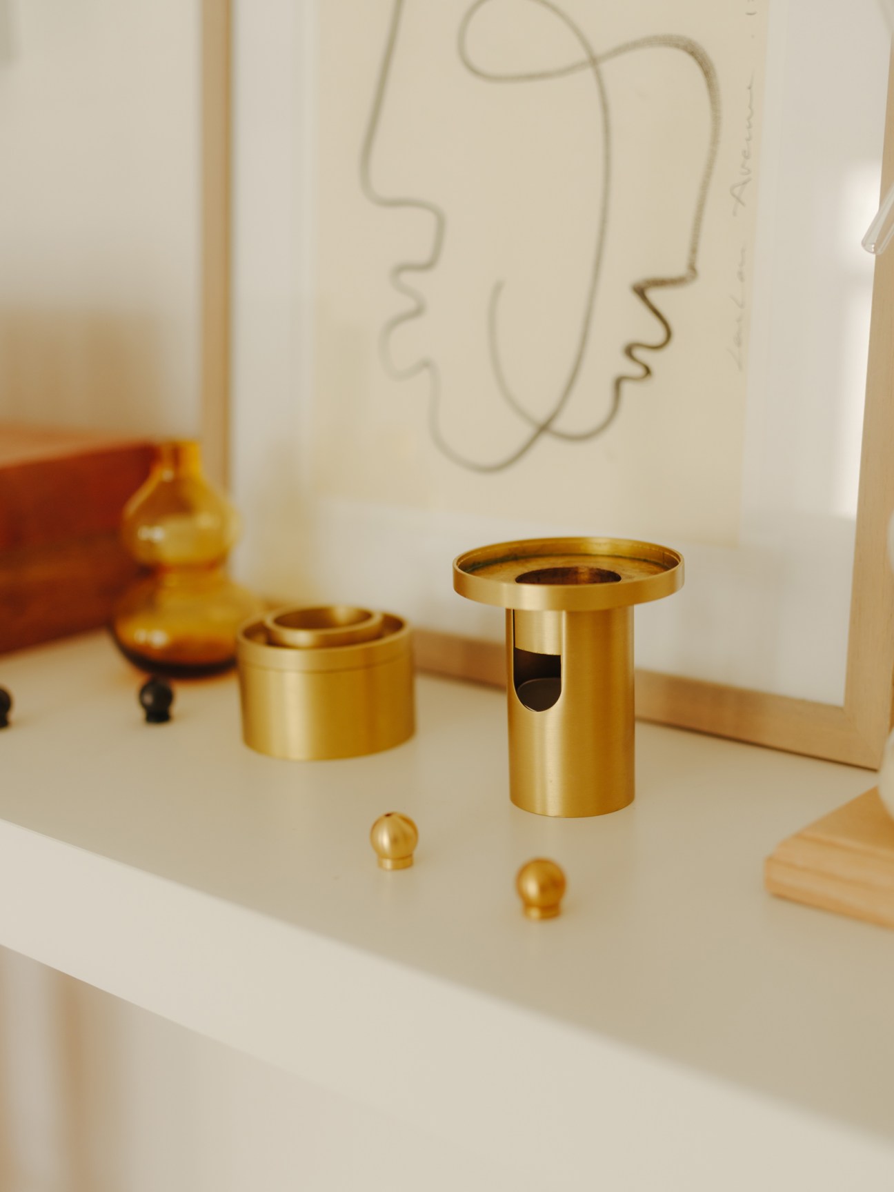 Gold brass oil burners and incense holders displayed on a white surface with abstract line art.