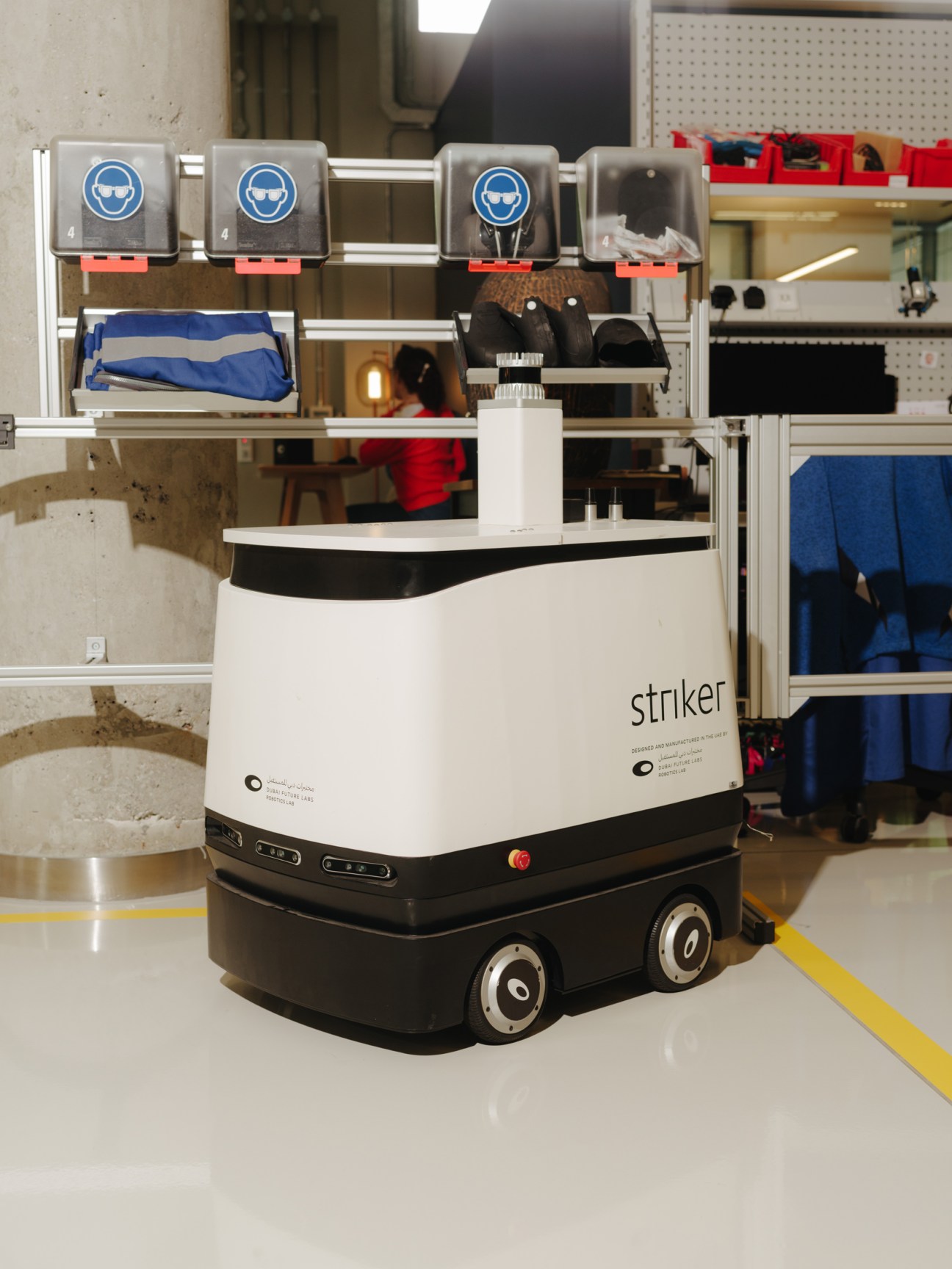 A white and black ground-based robot labeled 'striker' in a laboratory setting with safety equipment storage above.