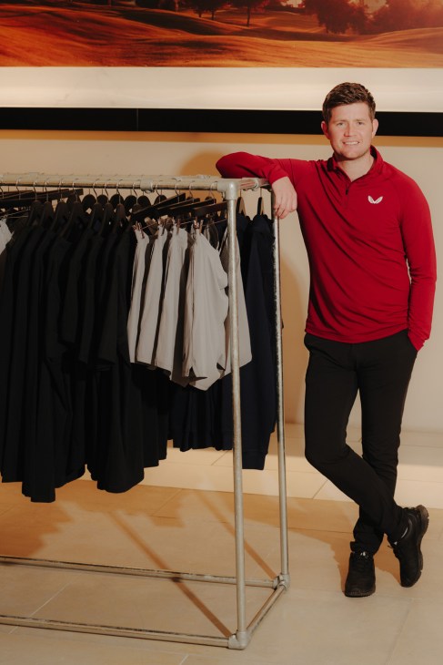 Tom Beahon, co-founder of Castore sportswear, stands next to a clothing rack displaying athletic wear.