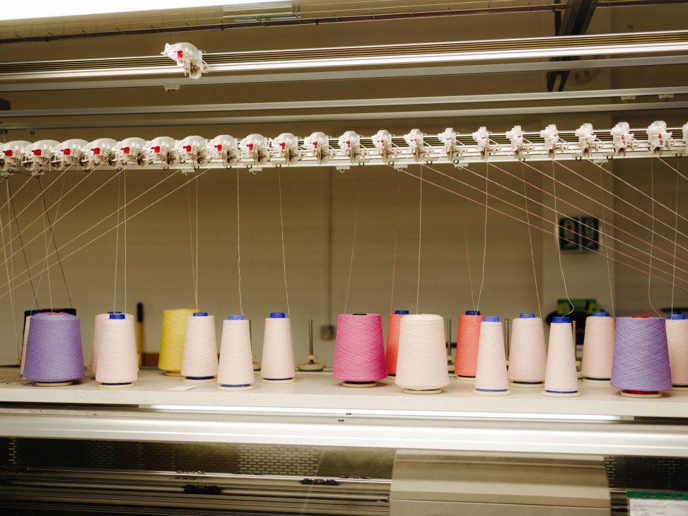 Electronic knitting machine with spools of colored yarn in purple, pink, yellow, and cream at Barrie factory.