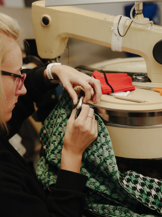 Worker stitching a green patterned cashmere garment on a sewing machine at Barrie factory.