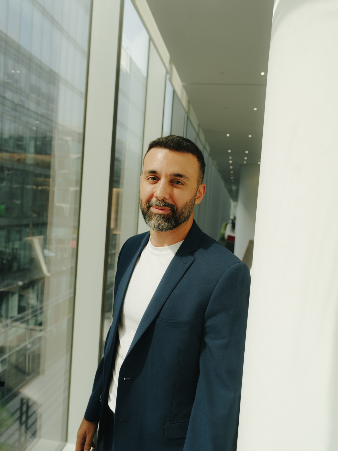 URB CEO Baharash Bagherian standing in a modern corridor wearing a dark blue blazer and white T-shirt.