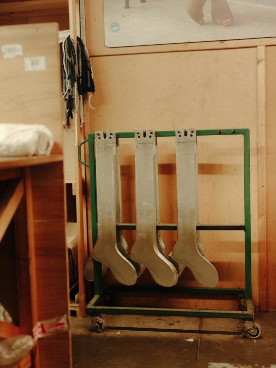 Industrial sock presses with cream-colored cashmere socks hanging on a green metal frame in a factory setting.