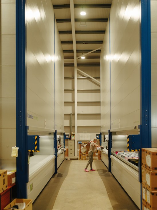 Interior of Johnstons' yarn store with high ceilings, blue structural columns, and shelving units along the sides.
