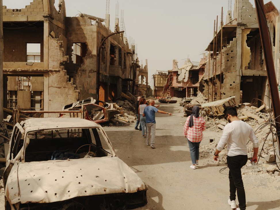 Visitors walking through a war-torn film set with destroyed buildings, damaged cars and rubble in Abu Dhabi's Twofour54 backlot.
