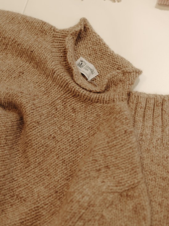 Close-up of a beige cashmere funnel neck sweater by Johnstons with visible label detail.