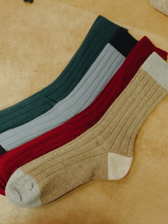 Steamed, pressed and finished cashmere socks in multiple colors arranged on a beige surface.