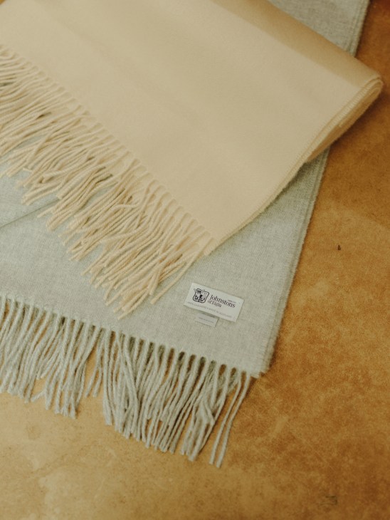 Fine cashmere scarves with fringed edges by Johnstons, displayed in neutral cream and caramel tones.