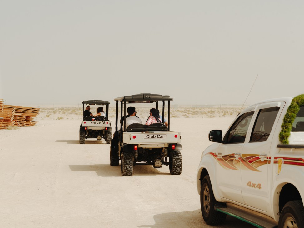 Club Car golf buggies touring a desert film set with passengers, accompanied by a white 4x4 vehicle nearby.