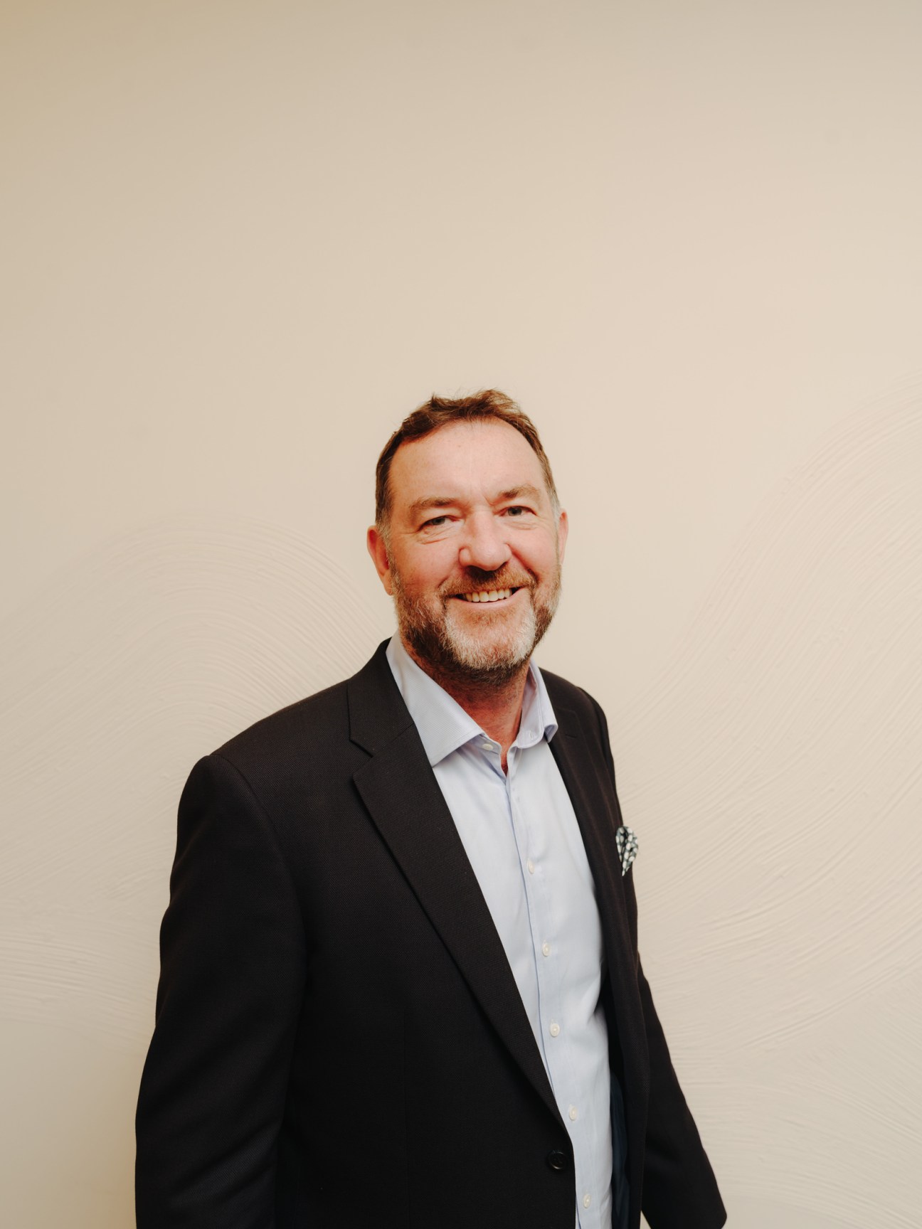 Mark Whitehead, CEO of Twofour54, wearing a black blazer and light blue shirt, smiling at the camera against a neutral beige background.