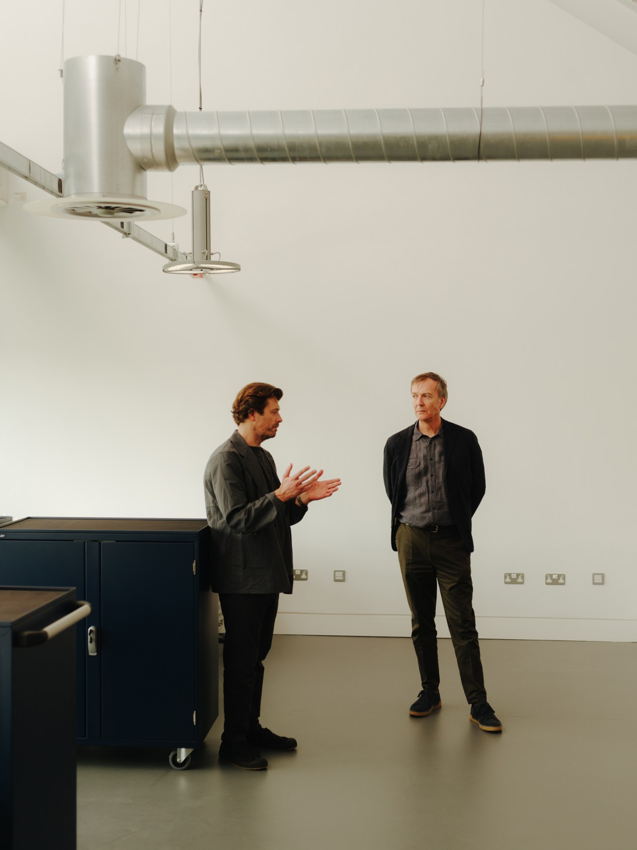 Two men in conversation inside the new RCA Rausing Research and Innovation Building with exposed ceiling ducts