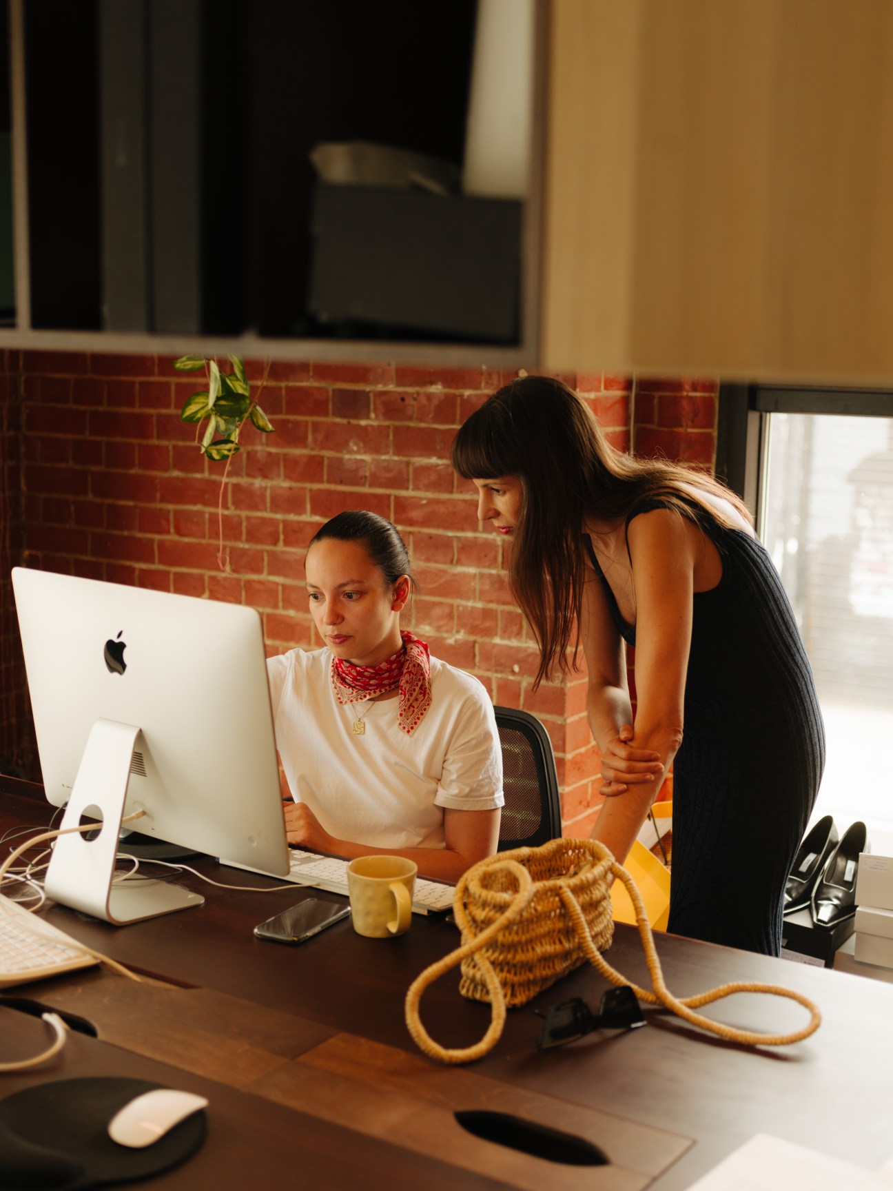 Two women working at desk with computer and yellow knitted bag in modern office space