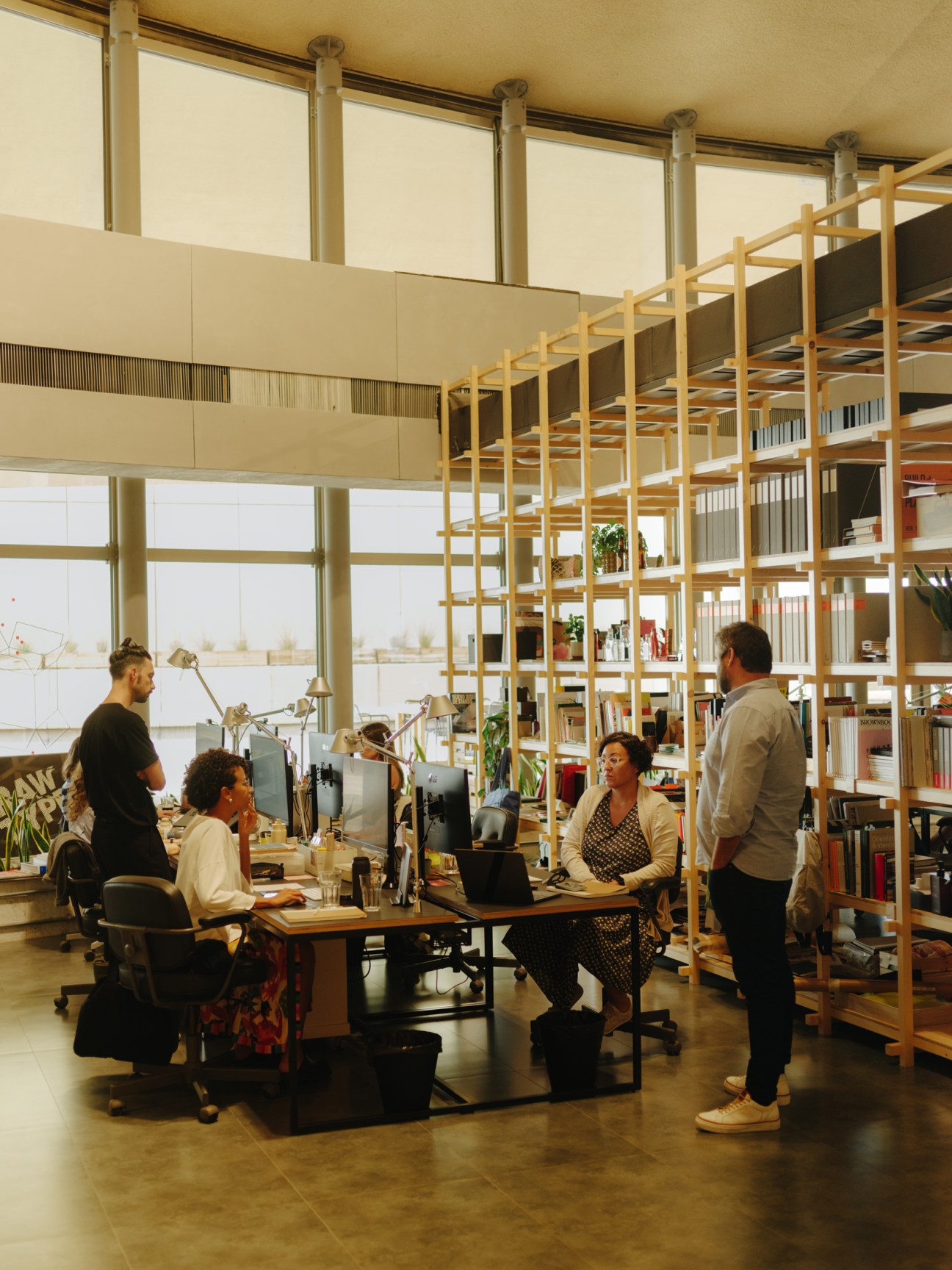 Interior of Slash design studio with five people working at desks near large windows and wooden shelving.