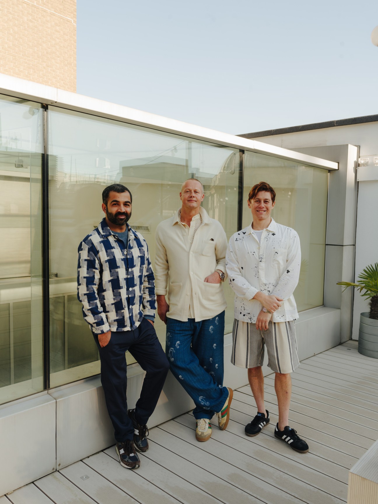 Three men posing on a rooftop terrace in casual clothing with patterned and embroidered designs.