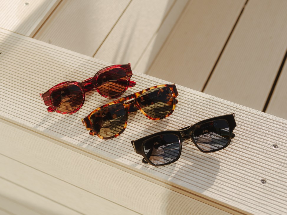 Three pairs of colorful sunglasses arranged on a light wooden surface.