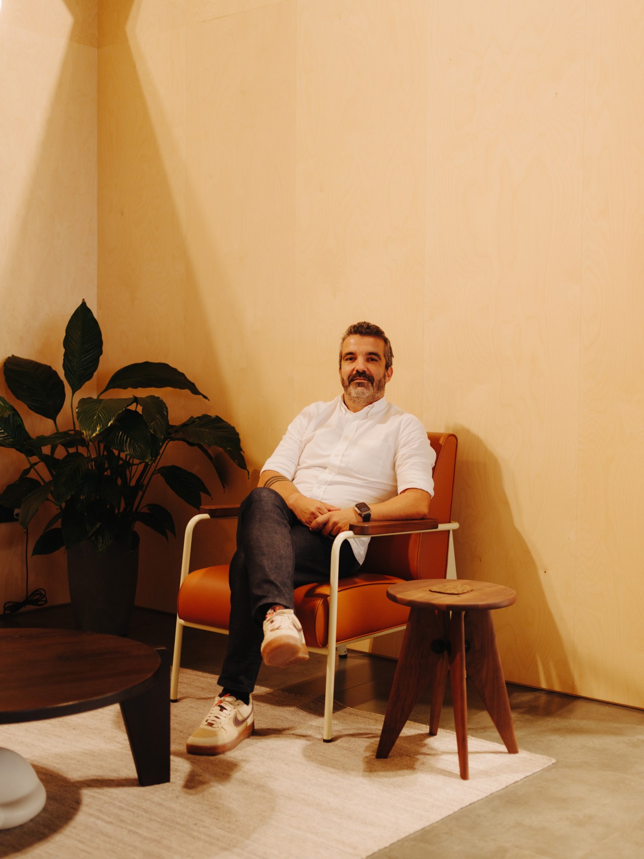 Man sitting in orange chair next to plant in minimalist interior space