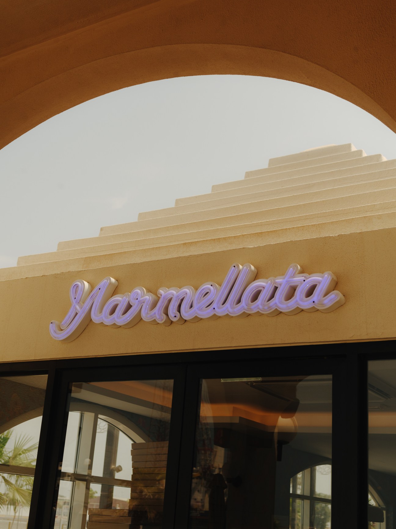 Purple neon 'Marmellata' sign on beige storefront with stepped architectural detail above.