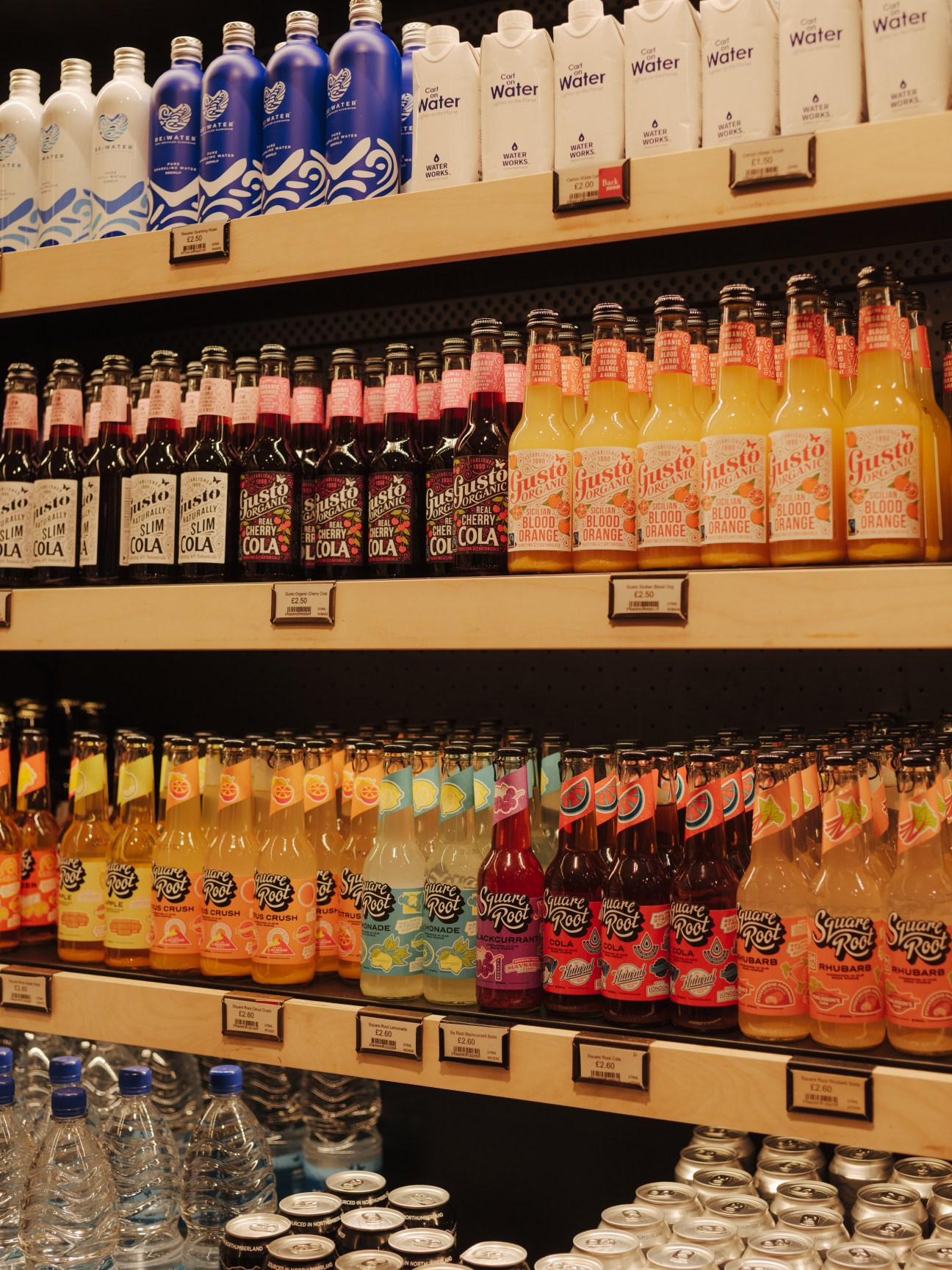 Shelves of bottled beverages including water, cola, and fruit juices at Gloucester Services.