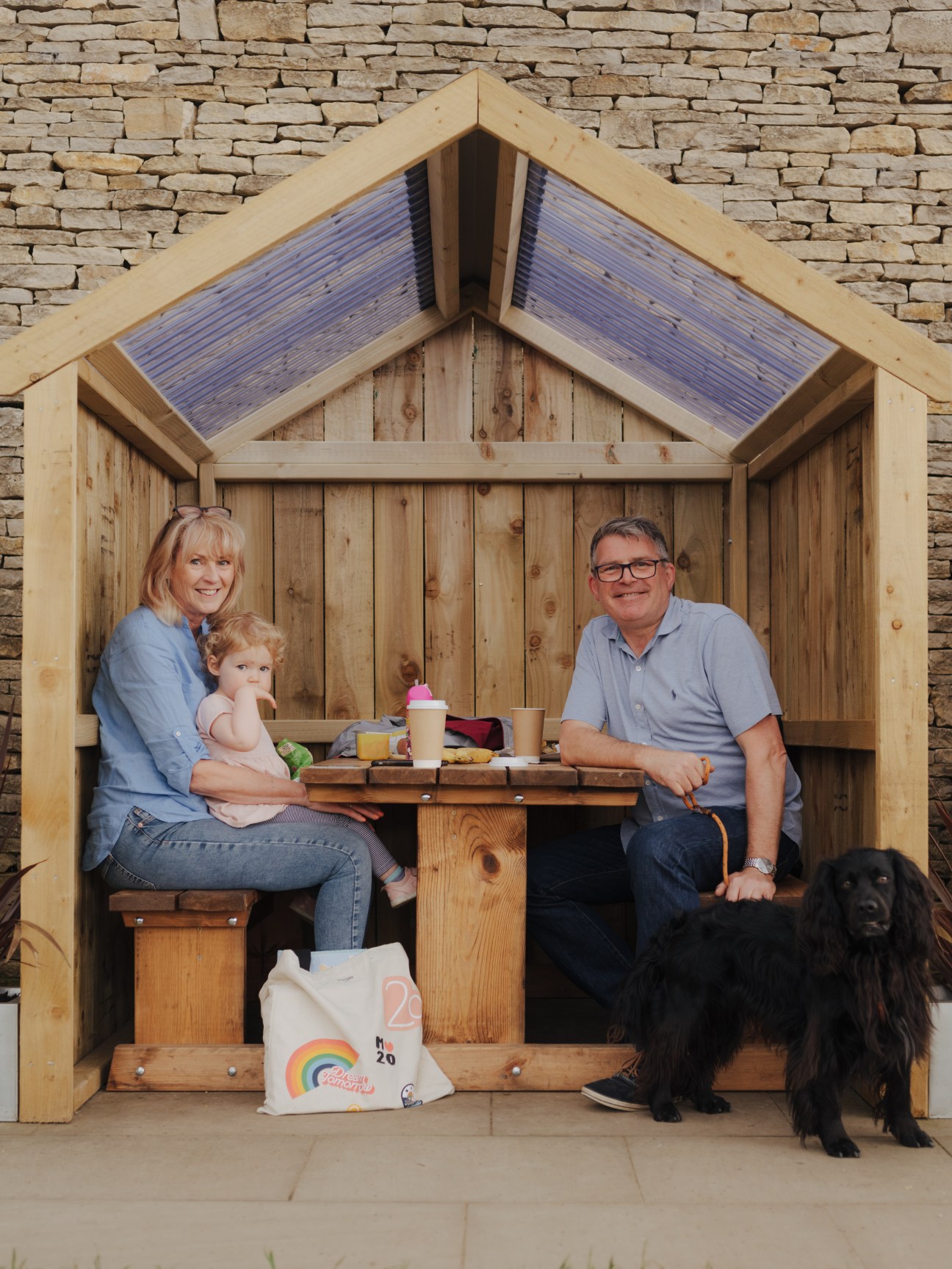 Family with child and dog sitting in wooden outdoor pod at Gloucester Services.