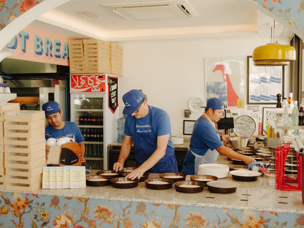 Marmellata founder Raj Dagstani and two staff members prepare pizzas behind the counter in blue branded uniforms.