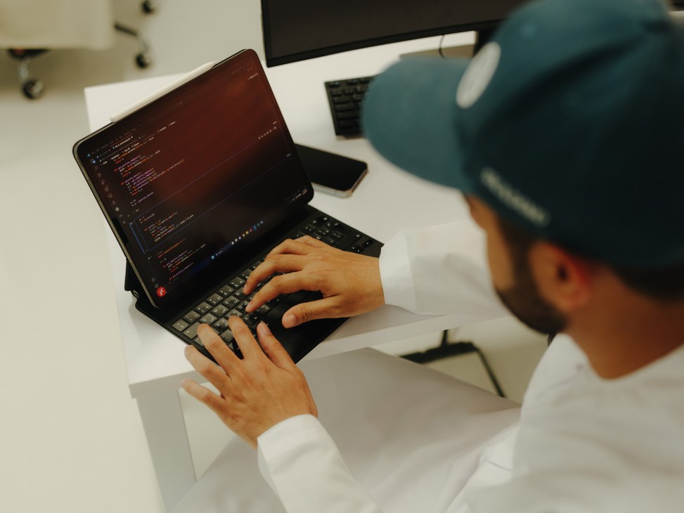 Developer typing code on a laptop displaying programming script in an open lab workspace.