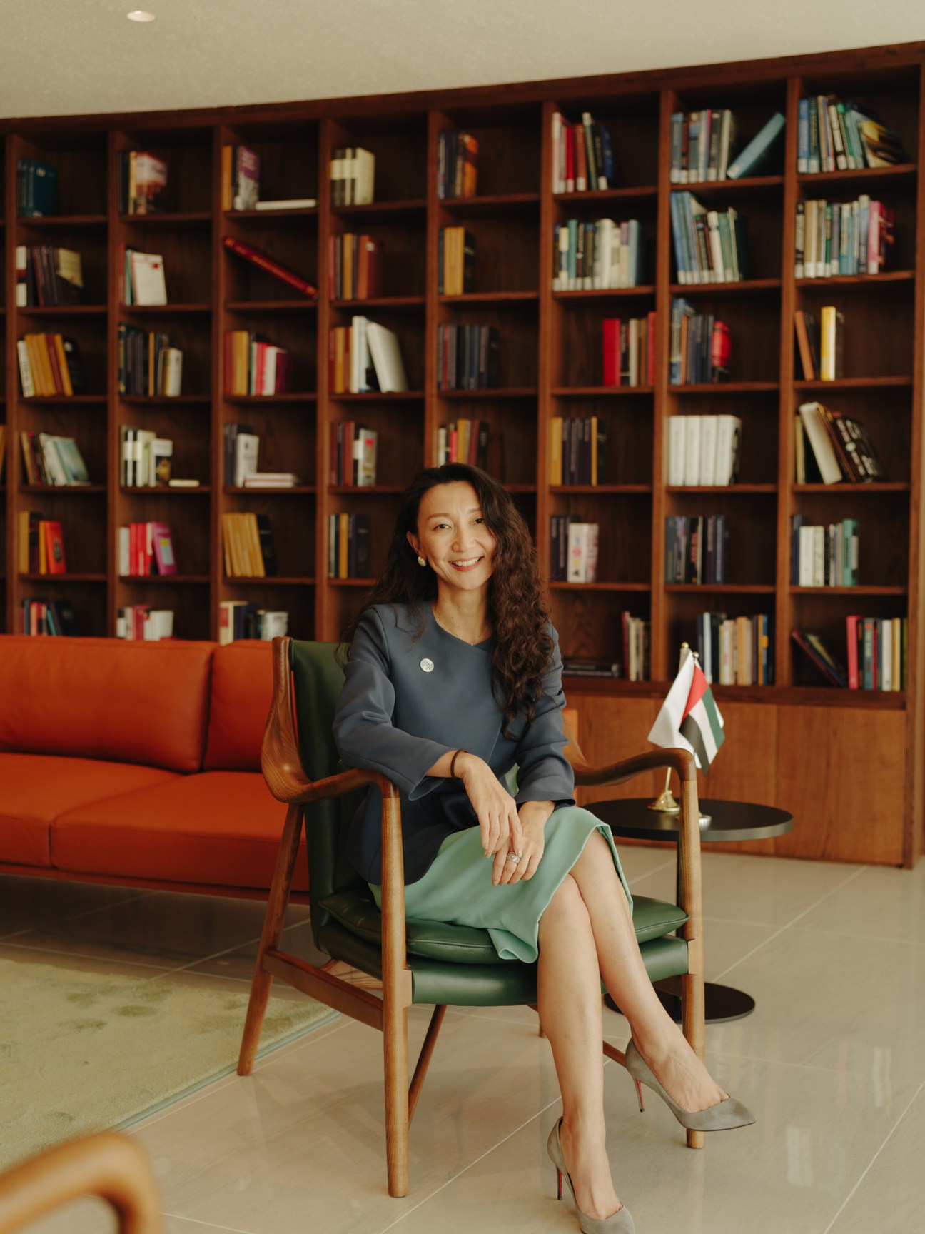 Dekyi Liang, chief of staff at Mohamed bin Zayed University of Artificial Intelligence, seated in a modern lounge with floor-to-ceiling wooden bookshelves and an UAE flag.