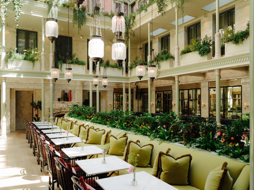 Nomad hotel's courtyard restaurant with long dining tables, green banquettes, hanging lanterns and climbing plants.