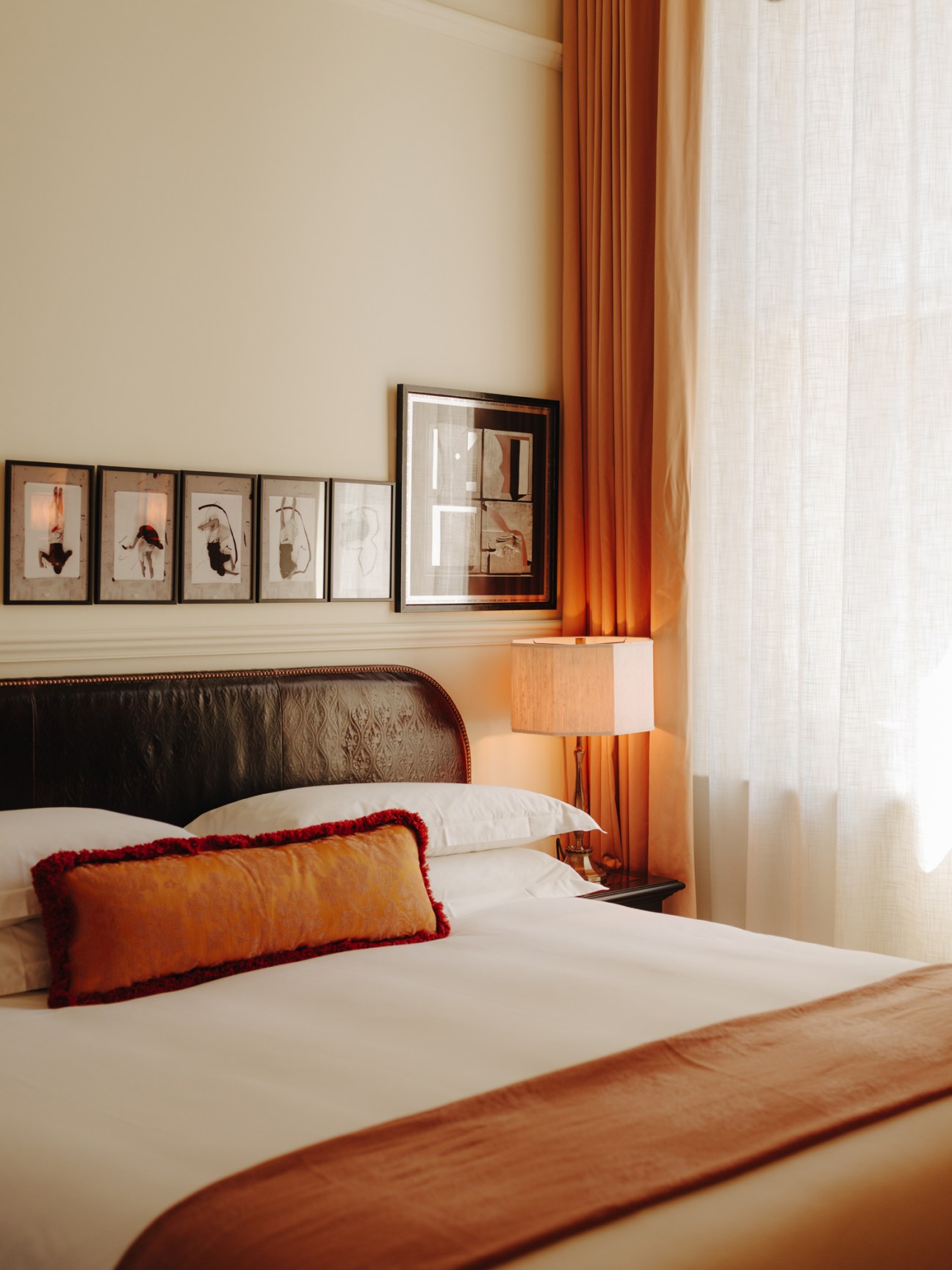 Nomad hotel bedroom with framed artwork, orange curtains, and decorative pillow on bed.