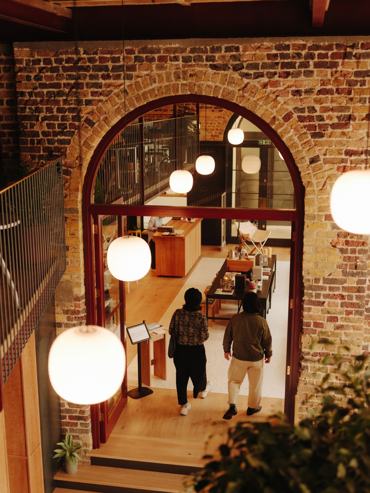 Modern interior with exposed brick archway, spherical pendant lights, and two people walking through retail space