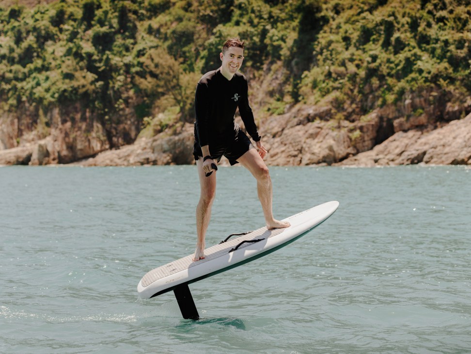 Person balancing on an e-foil board hovering above clear water surface