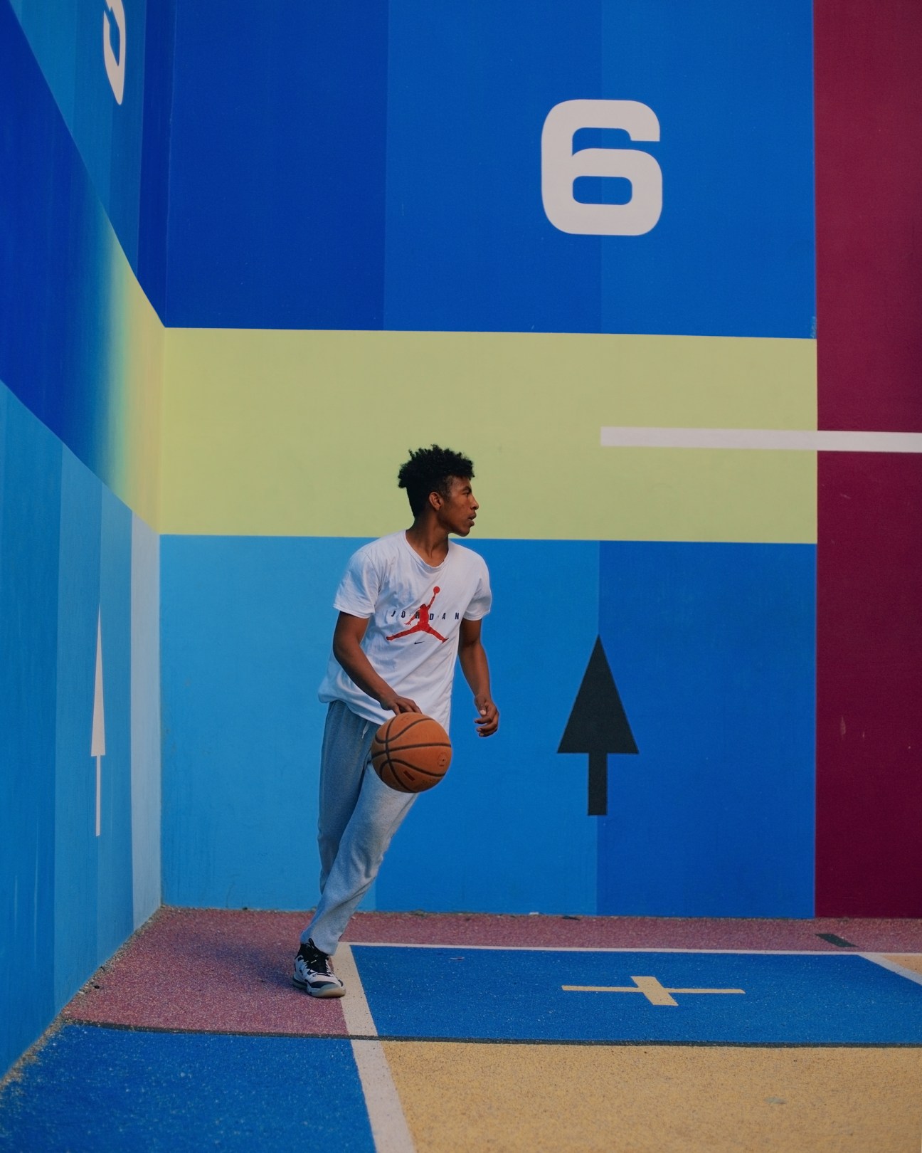 Young man in Jordan t-shirt dribbling basketball on vibrant blue and colorful court surface