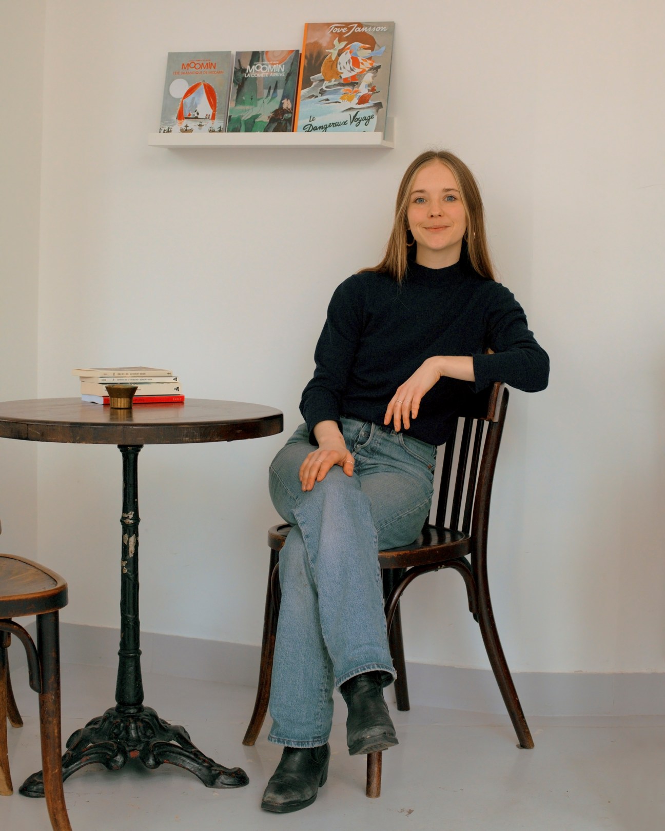 Woman sitting at table in Nordic bookshop with Swedish books displayed on wall shelf behind her