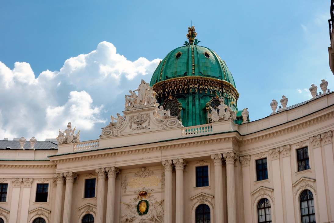 Historic Viennese palace with ornate baroque facade, green copper dome and classical columns under blue sky