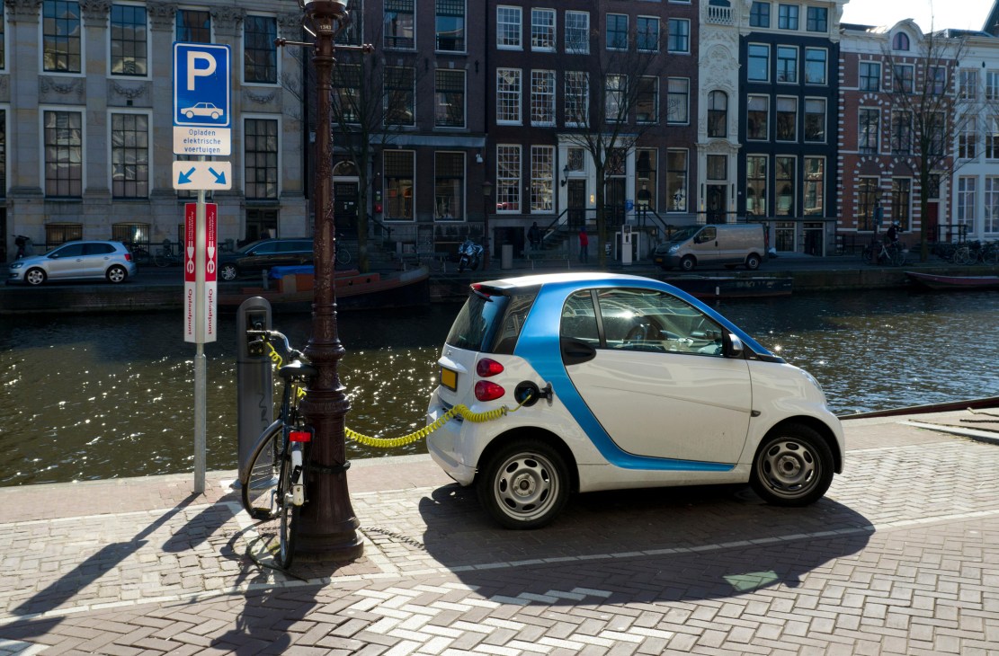 White and blue Smart electric car charging at a street pole beside an Amsterdam canal