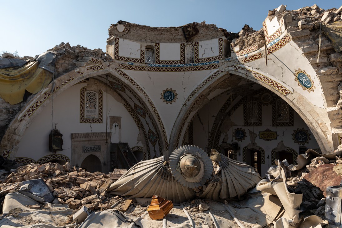 Ornate building with decorative arches severely damaged by earthquake, debris scattered in front.