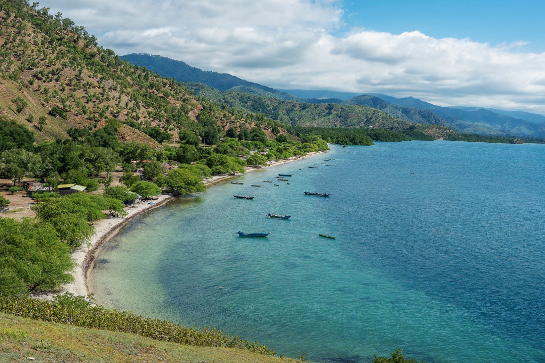 Aerial view of fishing boats anchored in turquoise bay waters near mountainous coastline with lush green vegetation