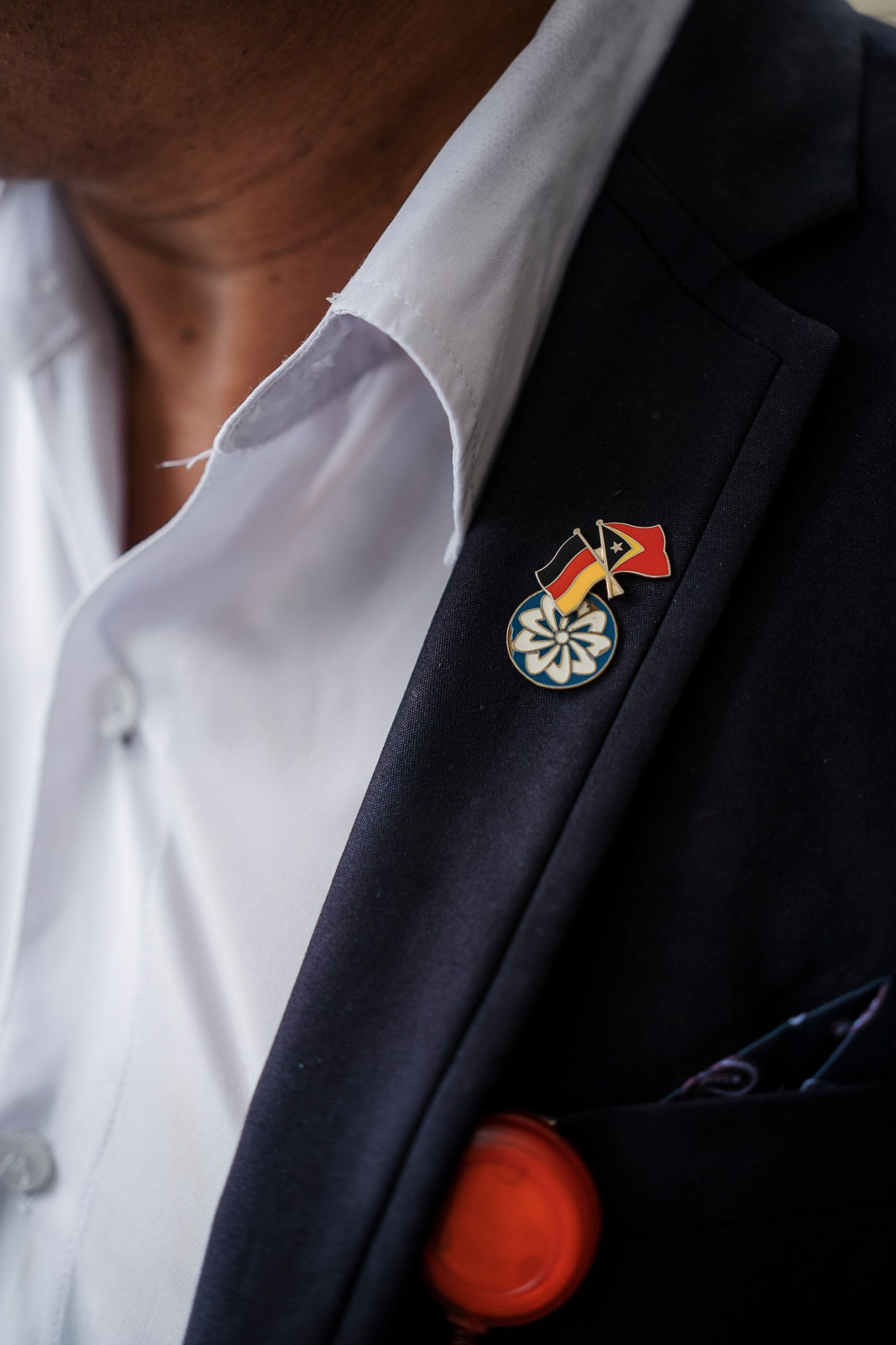 Close-up of a dark suit lapel with a pin featuring the Timor-Leste flag and what appears to be a medal or honor badge