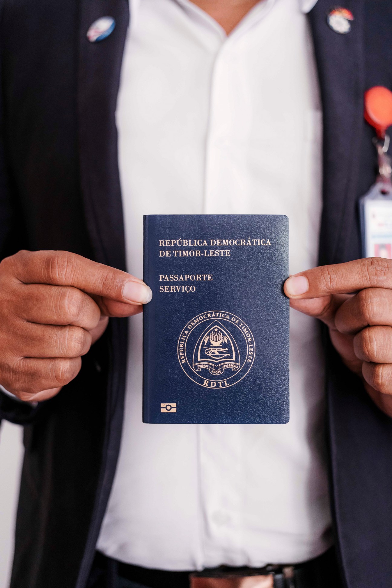 Hands holding a dark blue Timor-Leste service passport with the country's coat of arms